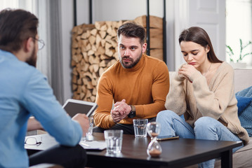 Annoyed caucasian couple of man and woman having conversation with psychologist on therapy session in light room.