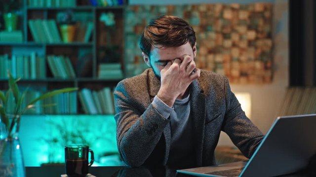 In front of the camera good looking office manager very tired with a sleepy face he working concentrated on the laptop and trying to not falling asleep at his work place in the office. 4k