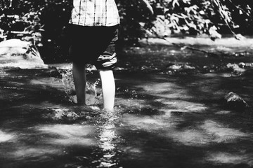 Child walking through creek water outdoors, childhood active lifestyle in black and white.