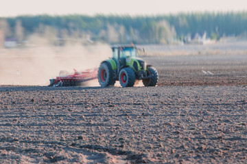 Tractor with a disc harrow system harrows the cultivated farm field, process of harrowing and...