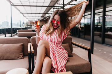 Magnificent girl in bright pink glasses spending summer day in cafe. Jocund fair-haired lady...