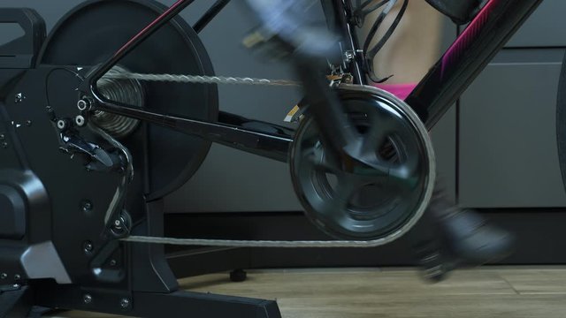 Female legs pedaling on stationary smart bicycle trainer. Chain, chainring, smart stationary cycling training at home. Cycling concept. Details of hain and chainring with rear cassette