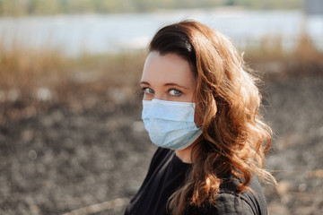 Portrait of woman wearing medical mask against the background of a river and scorched grass Coronavirus concept. Protect your health. 