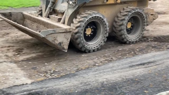 Construction equipment known as a skid steer clearing dirt from a road as it prepares for paving the street. 