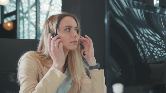 Sleepy bored young blonde woman with headset woken up by notification answering client's video chat call conversation on dekstop computer. Boring job and profession.