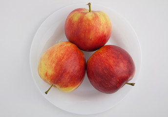 three red apples lie on a white plate on a white isolated background
