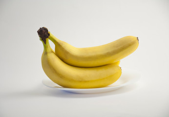 group of yellow bananas lies on a white plate on a white isolated background