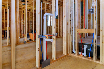 Applying pipe drain plumbing with hot red and cold blue pex pipe inside a house frame