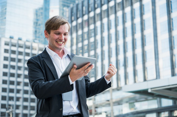 Young business man feeling happy celebration with hand and holding tablet