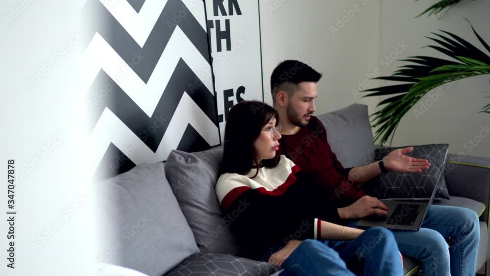 Poster couple in love relaxing together on cozy sofa and choosing app on modern laptop computer using wirel