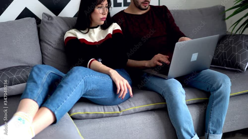 Poster young marriage relaxing together on comfortable couch and choosing movie on website on modern laptop