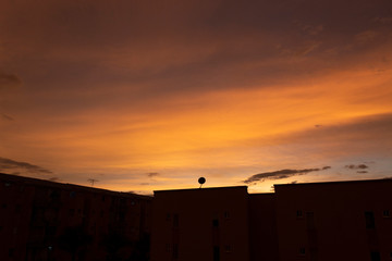 Stunning orange and yellow summer sunset with residential unit black silhouette and strange clouds formations
