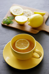 cup of tea with fresh yellow lemons on black background