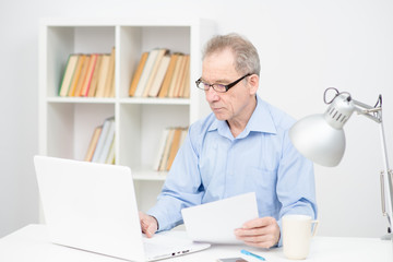 A male pensioner works with papers remotely behind a laptop at home. Stay home while quarantined