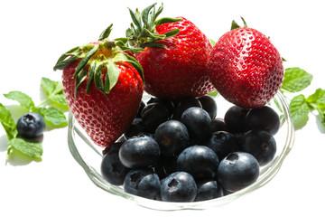 Ripe strawberries and blueberries in a glass vase on a white background . Topic healthy, vegan food, diet