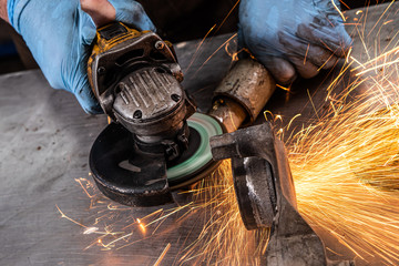 A young man welder in a blue gloves grinder metal an angle grinder   in the   workshop, sparks fly...