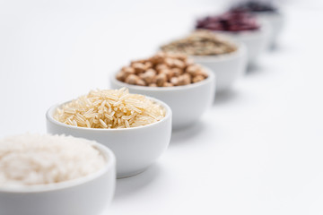 Grains of rice and beans background. Shallow depth of field on basmati rice grains in a white bowl with other types of rice cereals and bean legumes blurred in the background. Horizontal orientation.