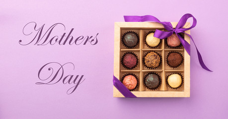 Set of different chocolates in a paper box with a satin ribbon on a bright background inscription Mother's Day.