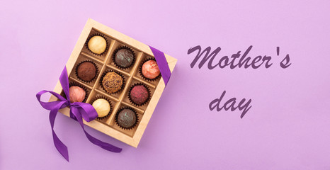 Set of different chocolates in a paper box with a satin ribbon on a bright background inscription Mother's Day.