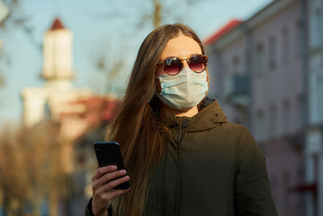 A woman with a smartphone wearing a medical face mask to avoid the spread coronavirus on a city...