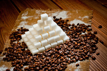 A pyramid made of refined sugar cubes and coffee grains, standing on a dark wooden surface.