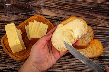 Someone spreads a little butter with a knife on fresh wheat toast, a piece of butter in a wooden...