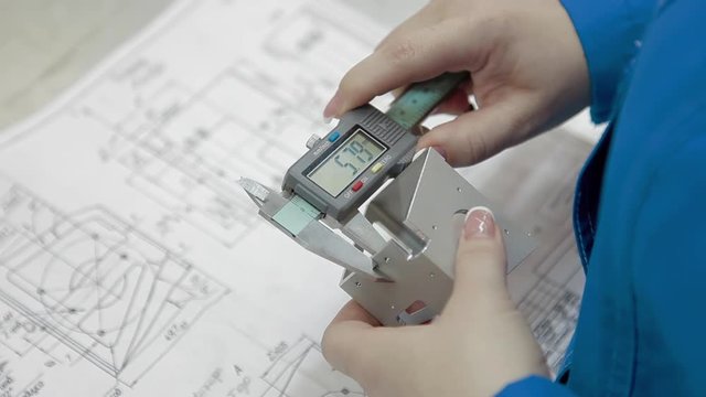 Engineer working in robe holding hands in an electronic caliper and measures the width of the metal part of the future device. High-precision equipment at factory.