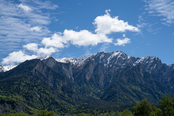 mountain landscape with jagged snow-covered peaks and green forest under an expressive blue sky