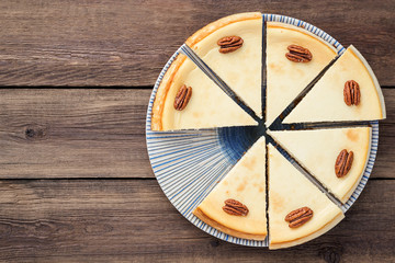 Sliced classic cheesecake with pecan nuts.