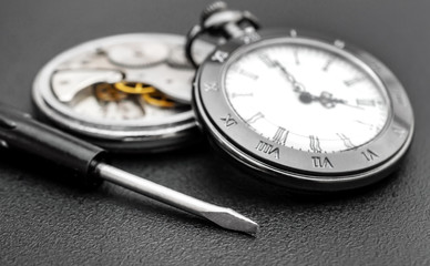 Broken pocket watch and new pocket watch with screwdriver on black background. Clockwork.