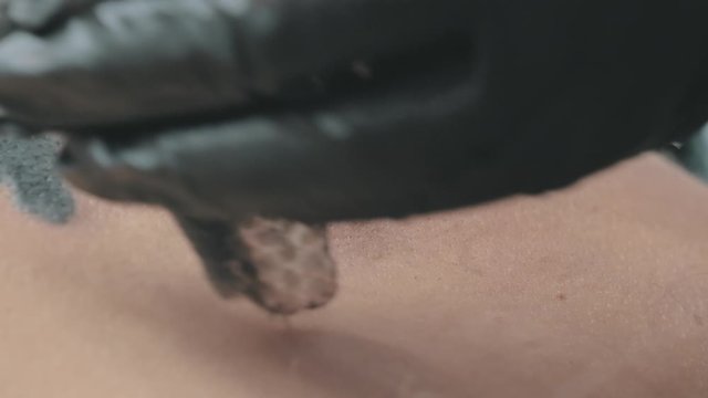 Needle tattoo machine injects ink into the skin of a girl. Tattoo artist puts a picture on a young woman's back. Professional tattooist works in studio. Slow motion, shallow depth of field.