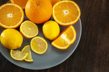 Fototapeta na wymiar Lemons and oranges on a plate on a dark wooden background (clouse-up)