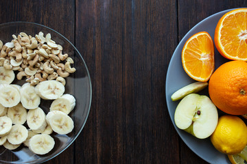 banana and cashew slices in a plate on a dark wooden background next to other fruits top view