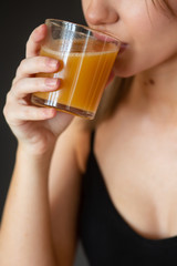 girl in sportswear drinks fresh orange juice on a dark background (close-up)