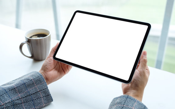 Mockup image of a woman holding black tablet pc with blank white screen with coffee cup on the table