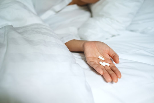 Closeup image of a sick woman sleeping and lying down on a bed with white pills in hand