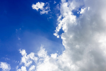 Bright fluffy clouds in deep blue sky with sun rays light
