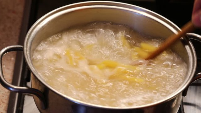 cook with wooden spoon mixes the pasta in boiling water in the pot