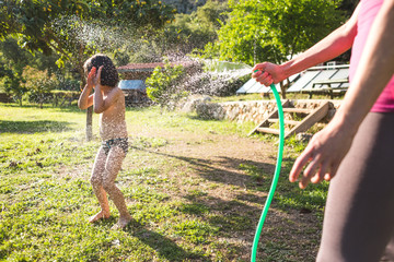 Boy splashed with water from a hose in the courtyard of the house on a hot sunny day.