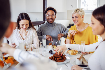 Small group of multiracial friends sitting at dinning table at home and having healthy food for lunch.