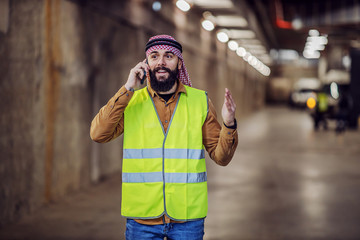 Smiling attractive bearded muslim investor in vest, with headscarf having conversation with...