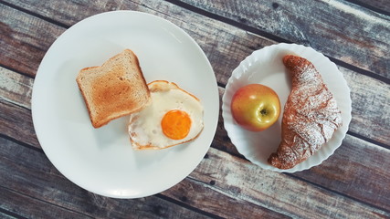 Healthy tasty breakfast: fried egg, toast, apple and croissant on table in kitchen