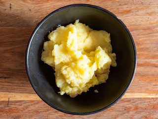top view of portion of mashed potatoes in black ceramic bowl on old wooden table in home kitchen