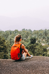 Woman tourist female with backpack is sitting on top of a mountain.