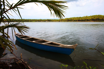 Naklejka na ściany i meble Lonely canoe on the riverbanks of Ponoor puzha. Aesthetic view of the Kerala beauty, depicting the elegance, serenity and harmony of the nature.