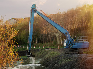 Blue excavator working on a river, Cleaning bottom. Warm sunny day, Cloudy sky, Heavy equipment in...