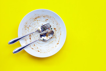 Dirty dish with spoon and fork on yellow background.
