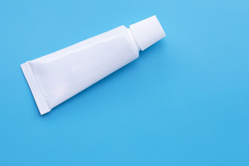 Small white toothpaste tube on blue background.