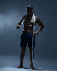 Healthy lifestyle. and Personal trainer  with strong body holds white belt. Guy poses in shorts  torso with belt. Man with confident face and bristle isolated on grey background