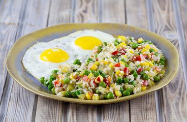 Rice with vegetables pepper, peas, corn and fried eggs on a plate. Place for text.